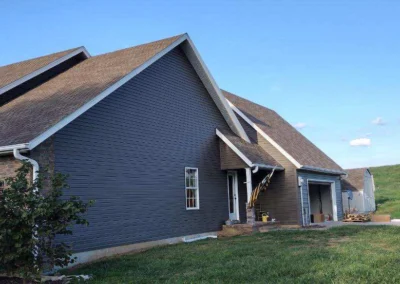 A contemporary gray and brick house with a sloped roof, situated on a grassy plot under a clear blue sky.